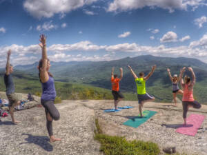  image of people doing yoga on a rock overlooking the mountains